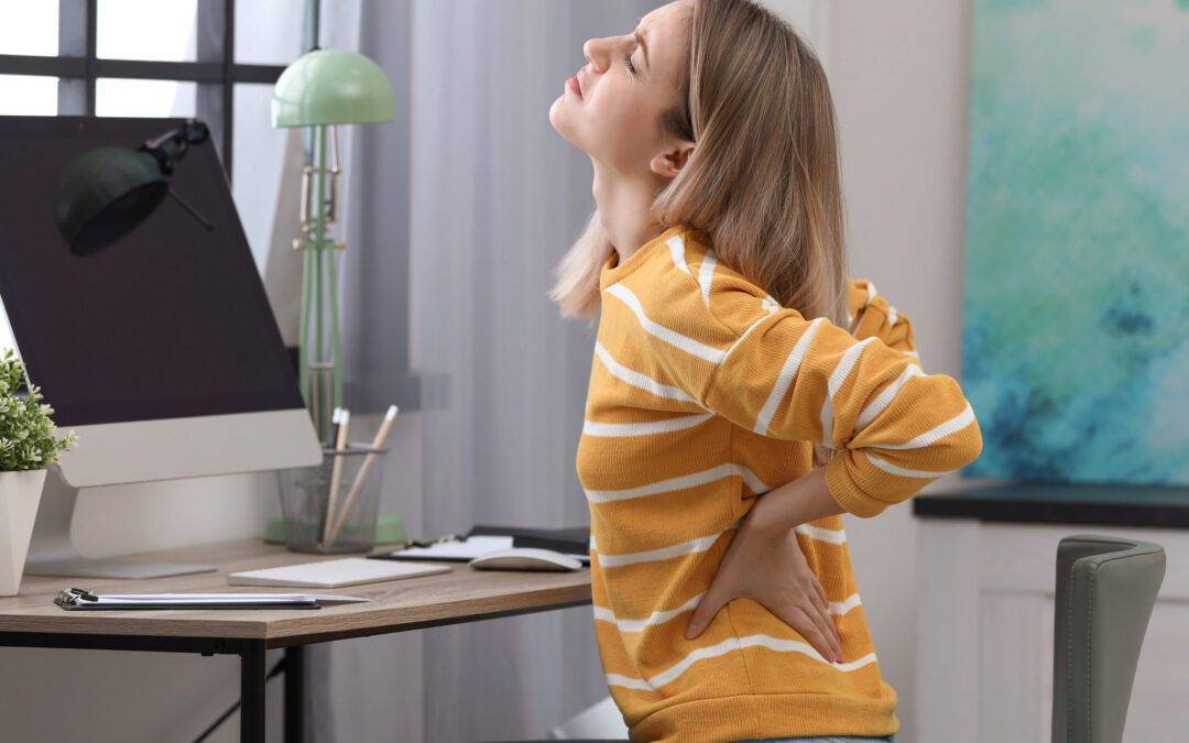 Young woman suffering from back pain in office