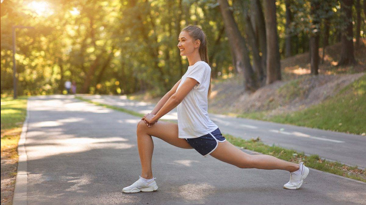 Woman runner stretching legs before exercising summer park morning